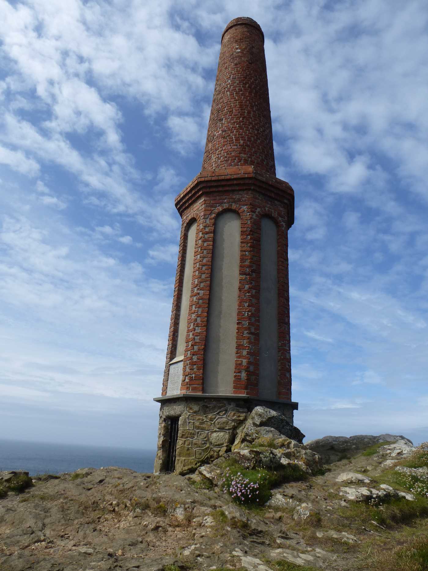 A tall cylindrical brick building on the cliff over looking the sea